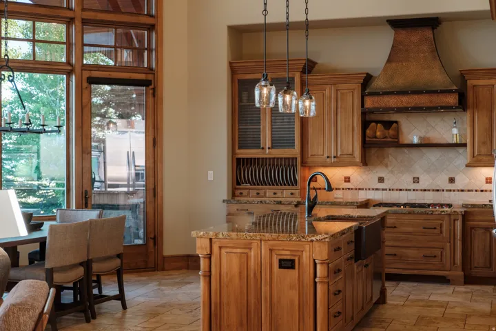 Gourmet kitchen featuring a central island with a farmhouse sink, pendant lighting, custom wood cabinetry, and a textured metal range hood