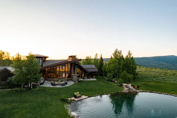 Contemporary rustic architecture featuring extensive window walls, a stone chimney, and a multi-level roofline