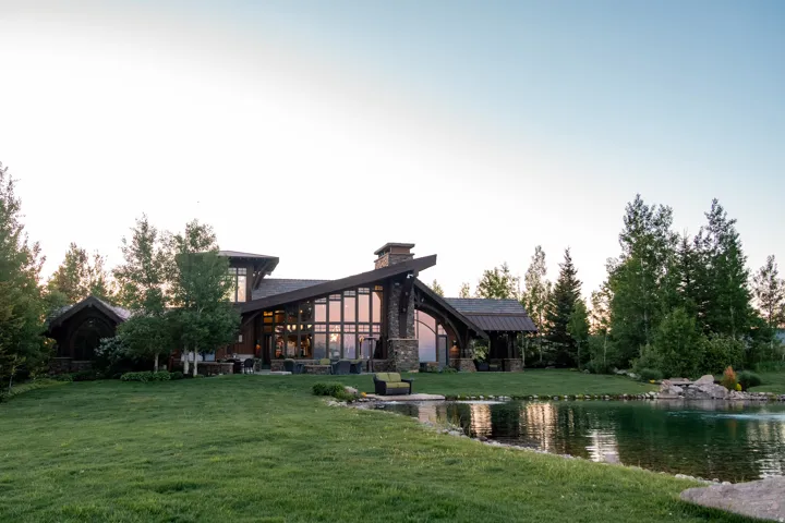 Modern architectural home featuring extensive glass paneling, a stone-clad chimney, and a multi-level roofline