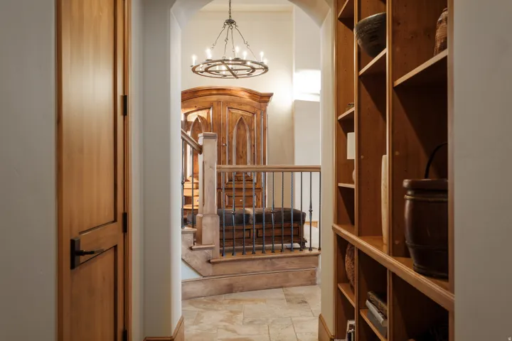 Arched entryway featuring an iron chandelier, built-in wooden shelving, natural wood doors, a wood staircase with iron balusters, and tiled flooring