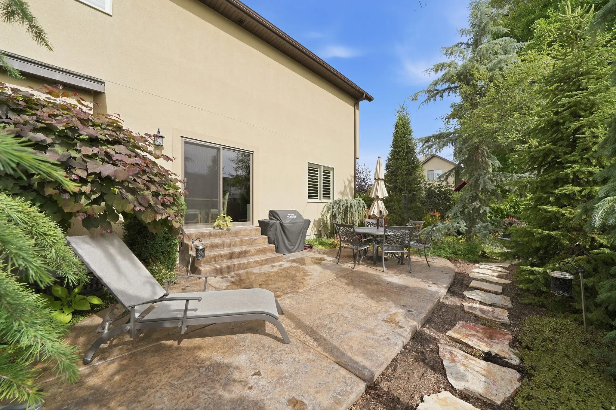 Stucco exterior with a concrete patio featuring steps to a sliding glass door