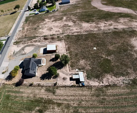Expansive property featuring a residence, detached outbuilding, gravel driveway, and surrounding undeveloped land