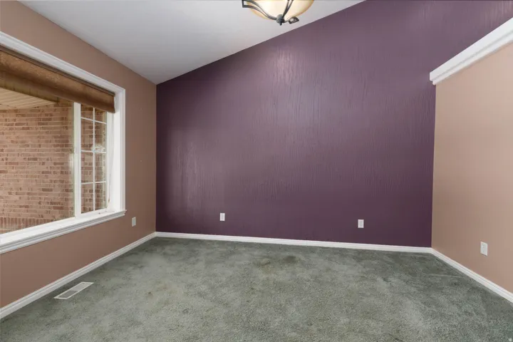 Vaulted ceiling with an overhead light fixture, a large window with white framing, and textured accent wall