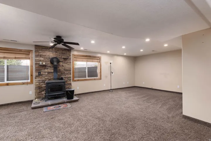 Spacious room featuring a stone-clad wood-burning stove with a stone hearth, natural wood window trim, and a ceiling fan