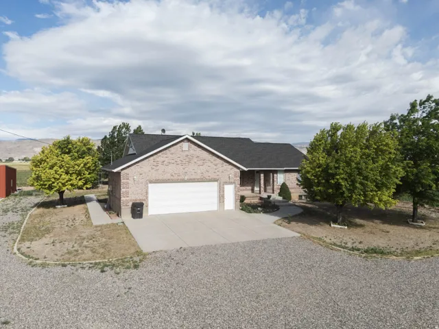 Brick exterior residence featuring a two-car garage, mature landscaping, and a gravel driveway