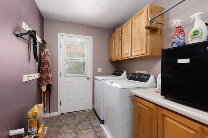 Utility room featuring tiled flooring, a white exterior door with window panes, and light wood-finish cabinetry