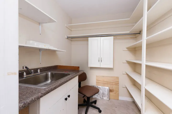 Utility room featuring a built-in sink with a countertop, white base cabinetry, wall-mounted upper cabinetry, and extensive shelving