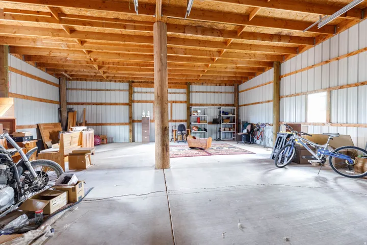 Spacious open-concept structure featuring exposed wood ceiling beams, concrete flooring, and multiple windows