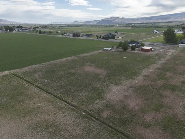 Expansive open land featuring a large green field, additional undeveloped acreage, and distant mountain ranges