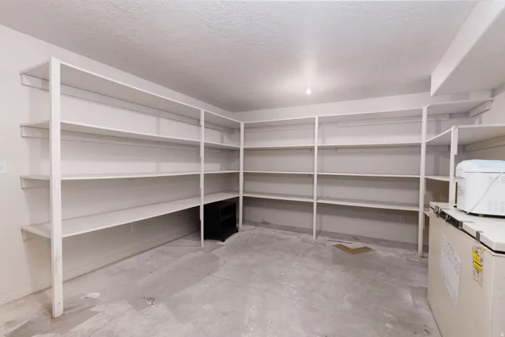 Spacious storage area featuring extensive built-in shelving, durable concrete flooring, and an overhead light fixture