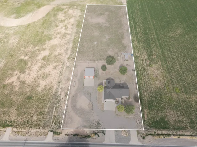Aerial view of a rectangular parcel featuring a single-story residence with a dark roof and a paved driveway