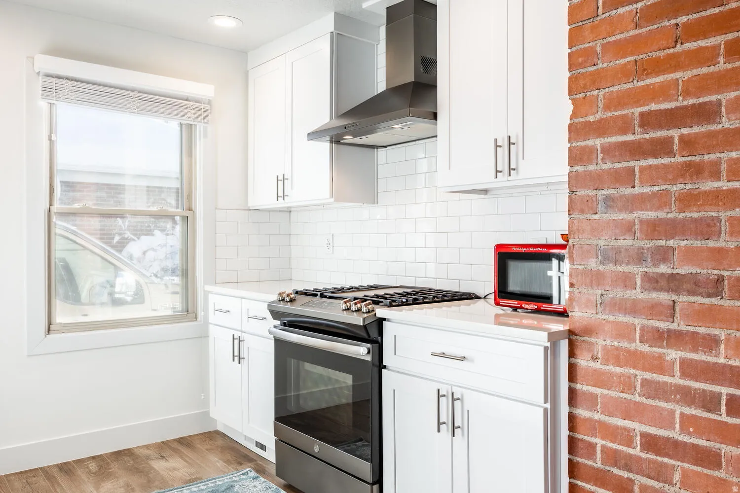 Modern kitchen featuring white shaker cabinetry, stainless steel appliances, subway tile backsplash, and a brick accent wall