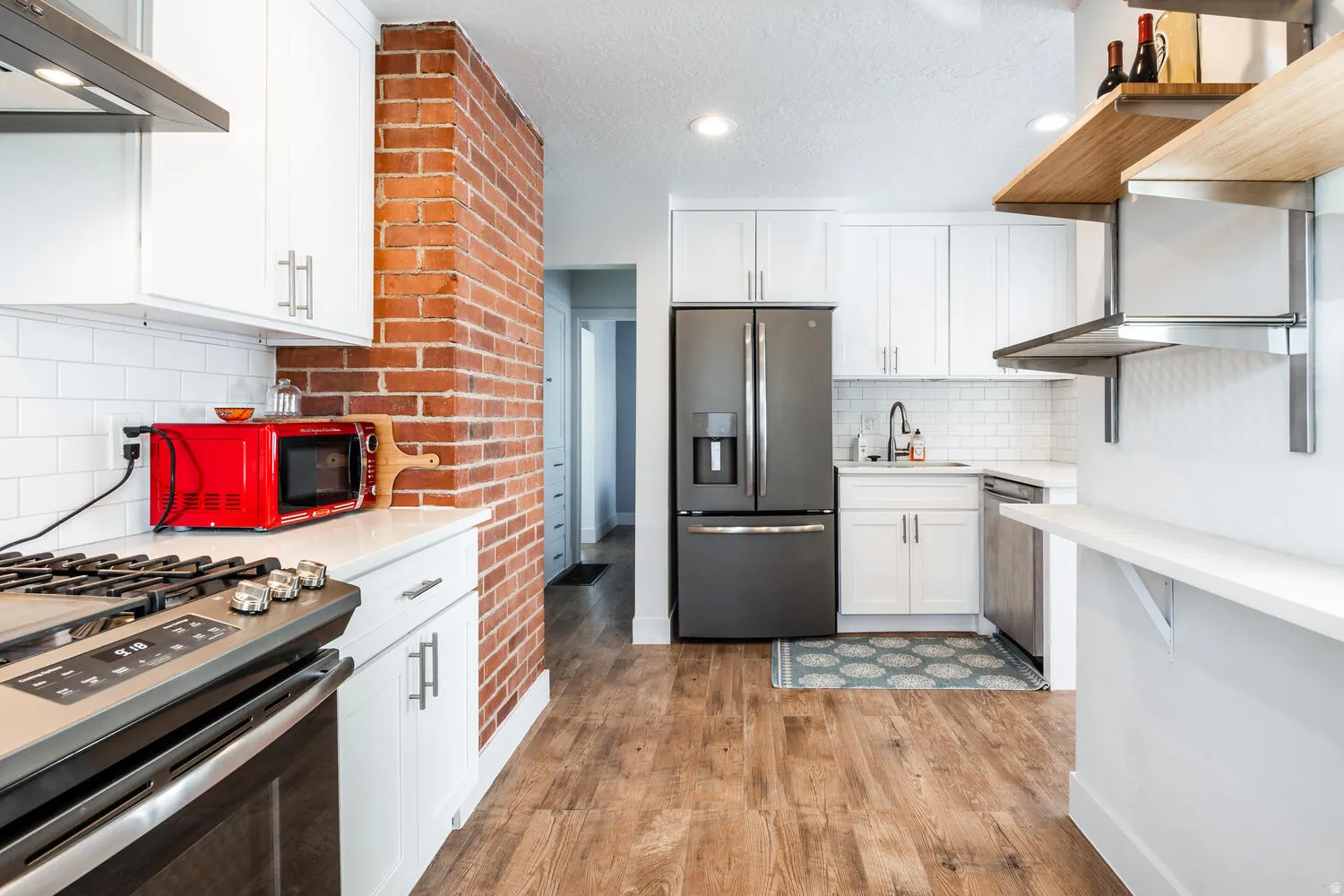 Kitchen featuring stainless steel appliances, white shaker cabinetry, wood-finish flooring, and a brick accent wall