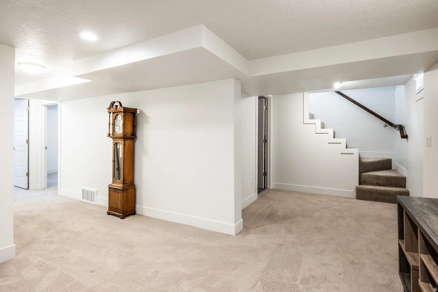 Expansive carpeted area featuring recessed lighting, a door opening to an additional room, and a staircase with a dark wood handrail