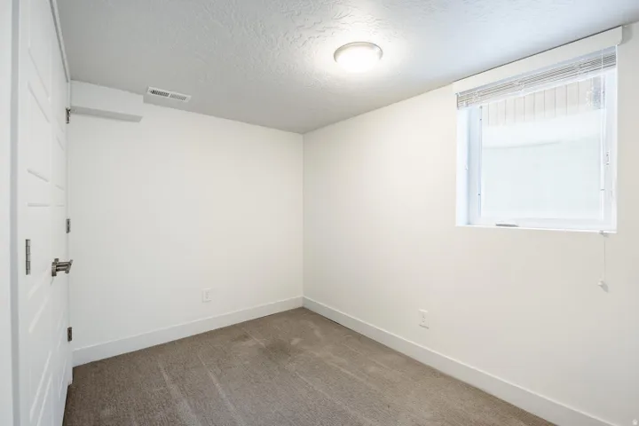 Carpeted room with white walls, a single window with blinds, and an overhead flush-mount light fixture
