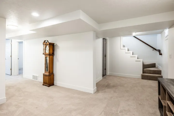 Expansive carpeted area featuring recessed lighting, a door opening to an additional room, and a staircase with a dark wood handrail