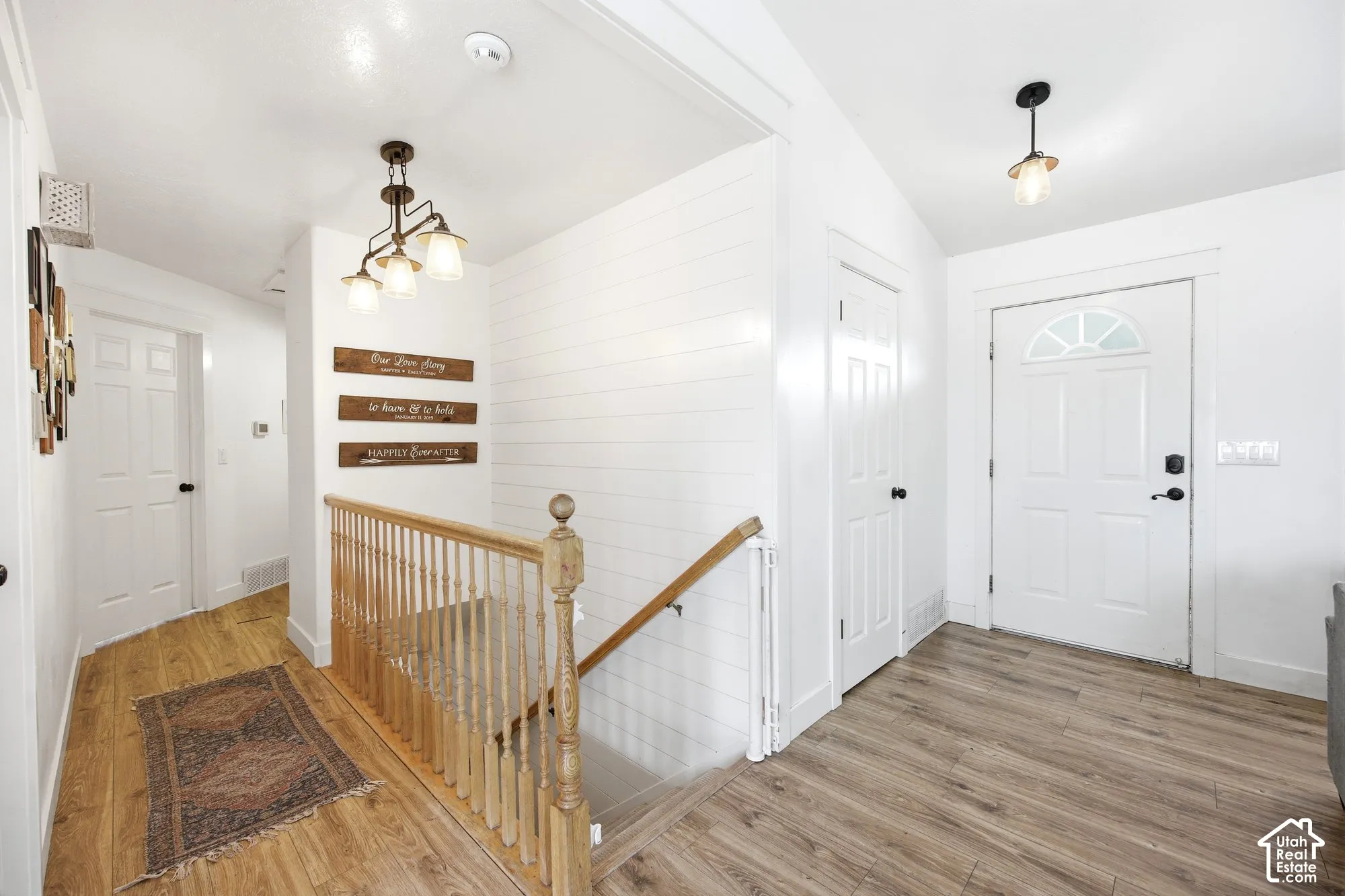 Entryway featuring wood-finish flooring, white shiplap accent wall, white paneled doors, and a staircase with a natural wood handrail and balusters