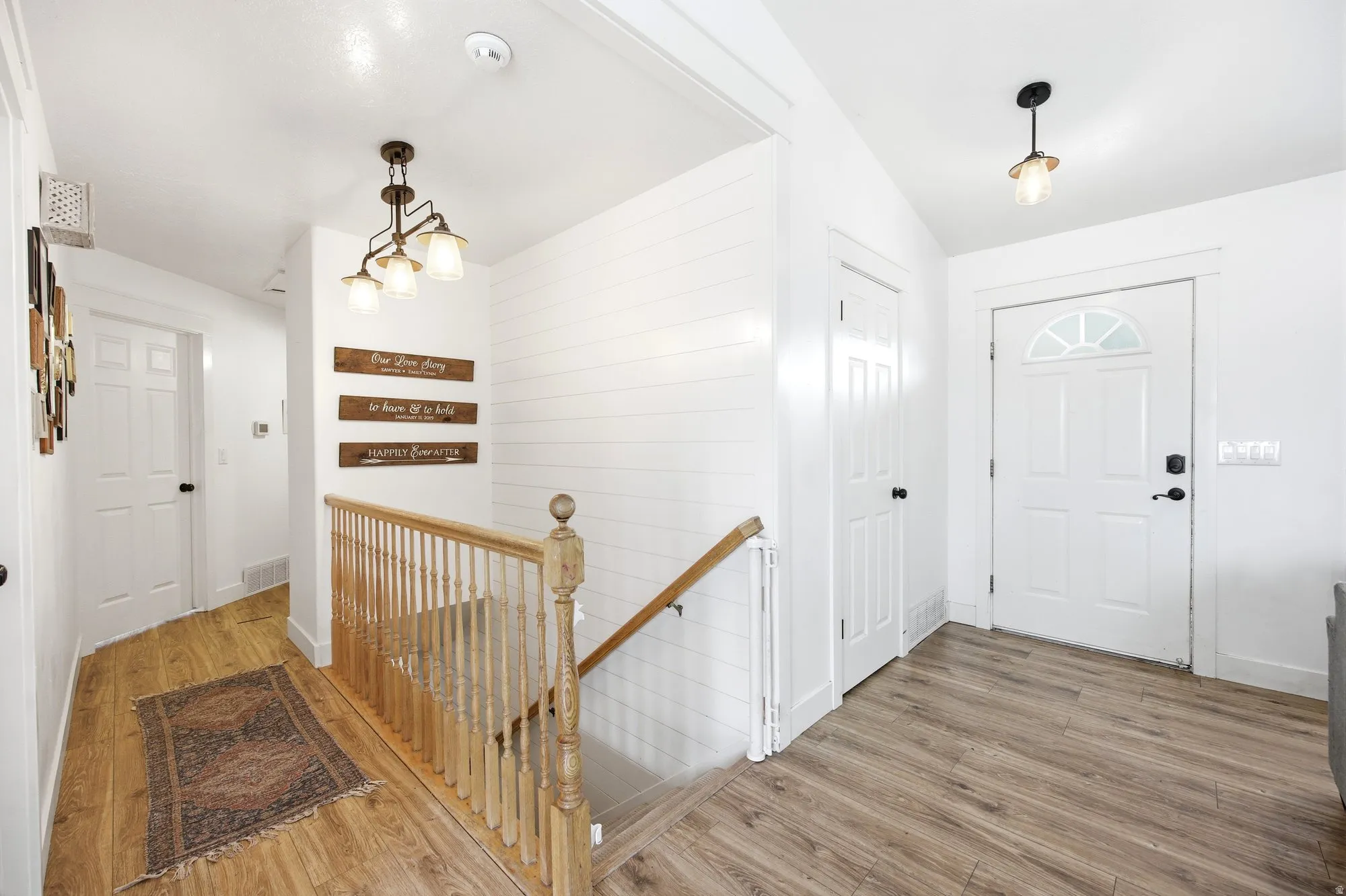 Entryway featuring wood-finish flooring, white shiplap accent wall, white paneled doors, and a staircase with a natural wood handrail and balusters