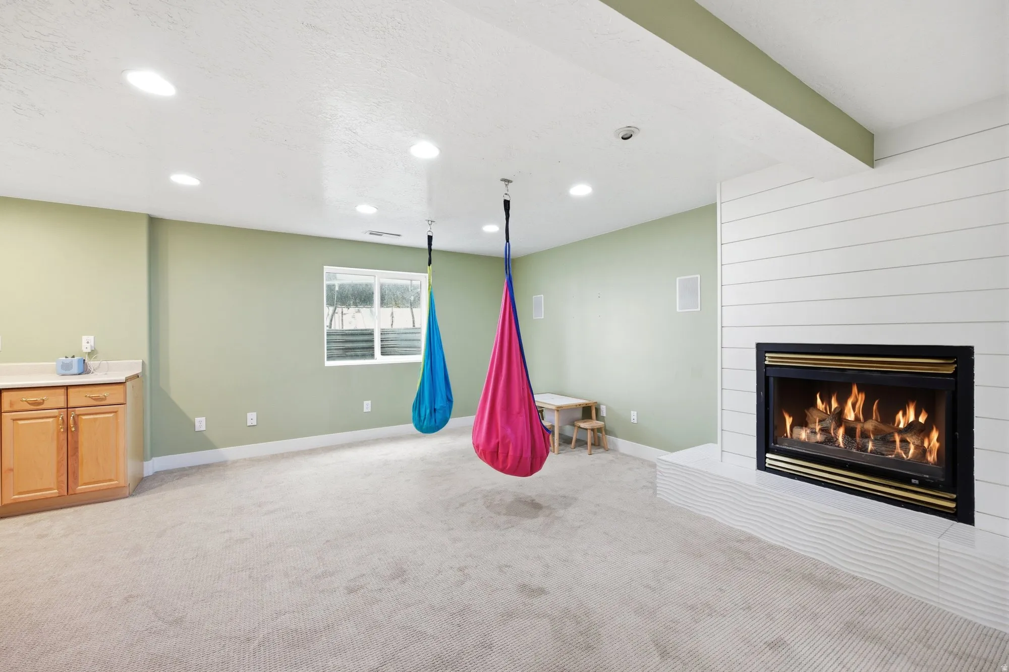 Spacious carpeted room featuring a white shiplap fireplace surround, built-in gas fireplace, recessed lighting, and a built-in counter with cabinetry