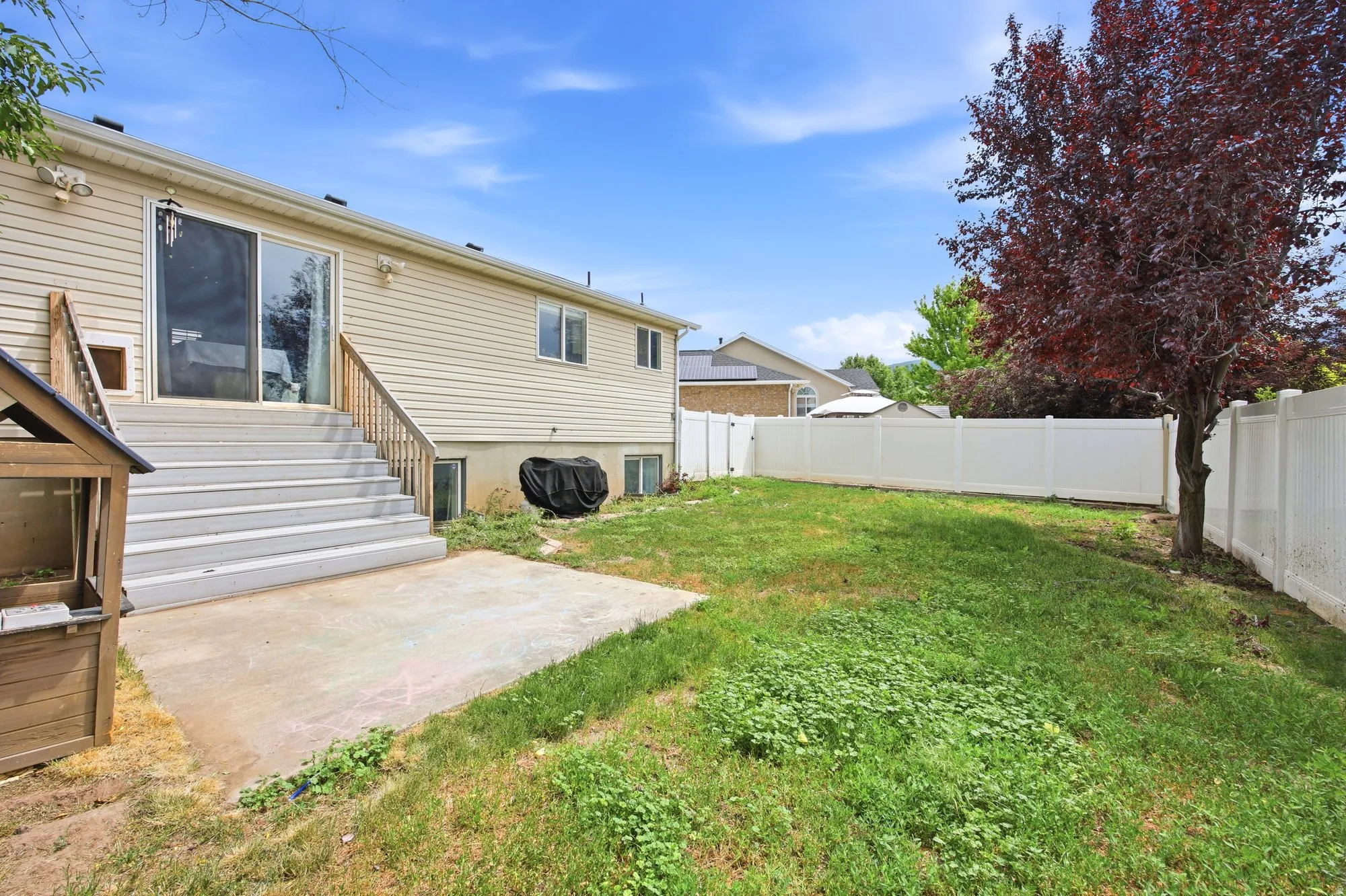 Expansive backyard featuring a concrete patio, wood deck with stairs, and a white privacy fence