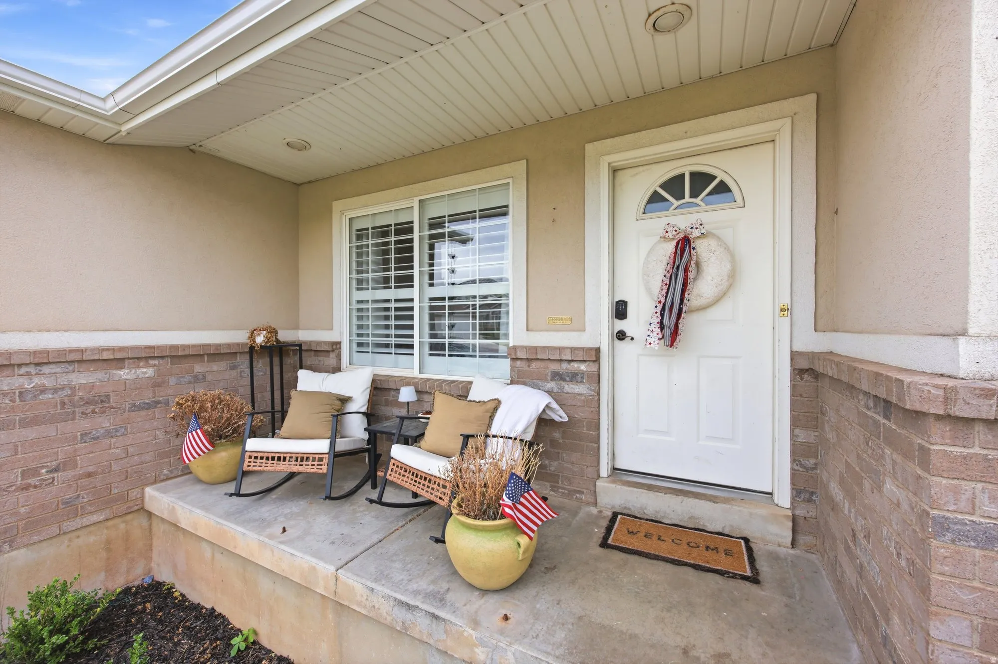 Covered porch featuring a brick facade and stucco exterior