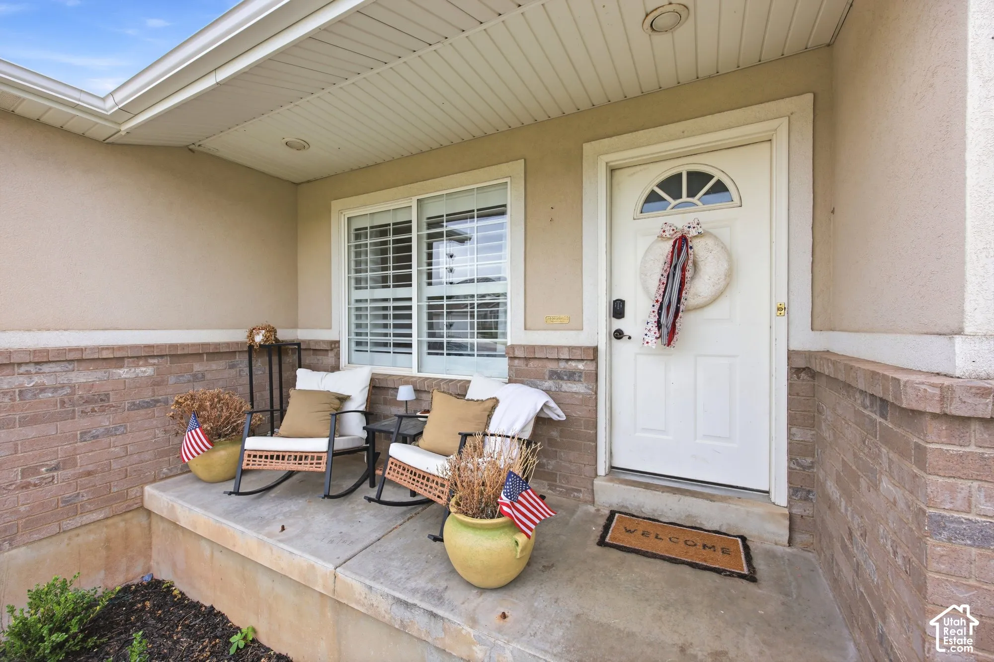 Covered porch featuring a brick facade and stucco exterior