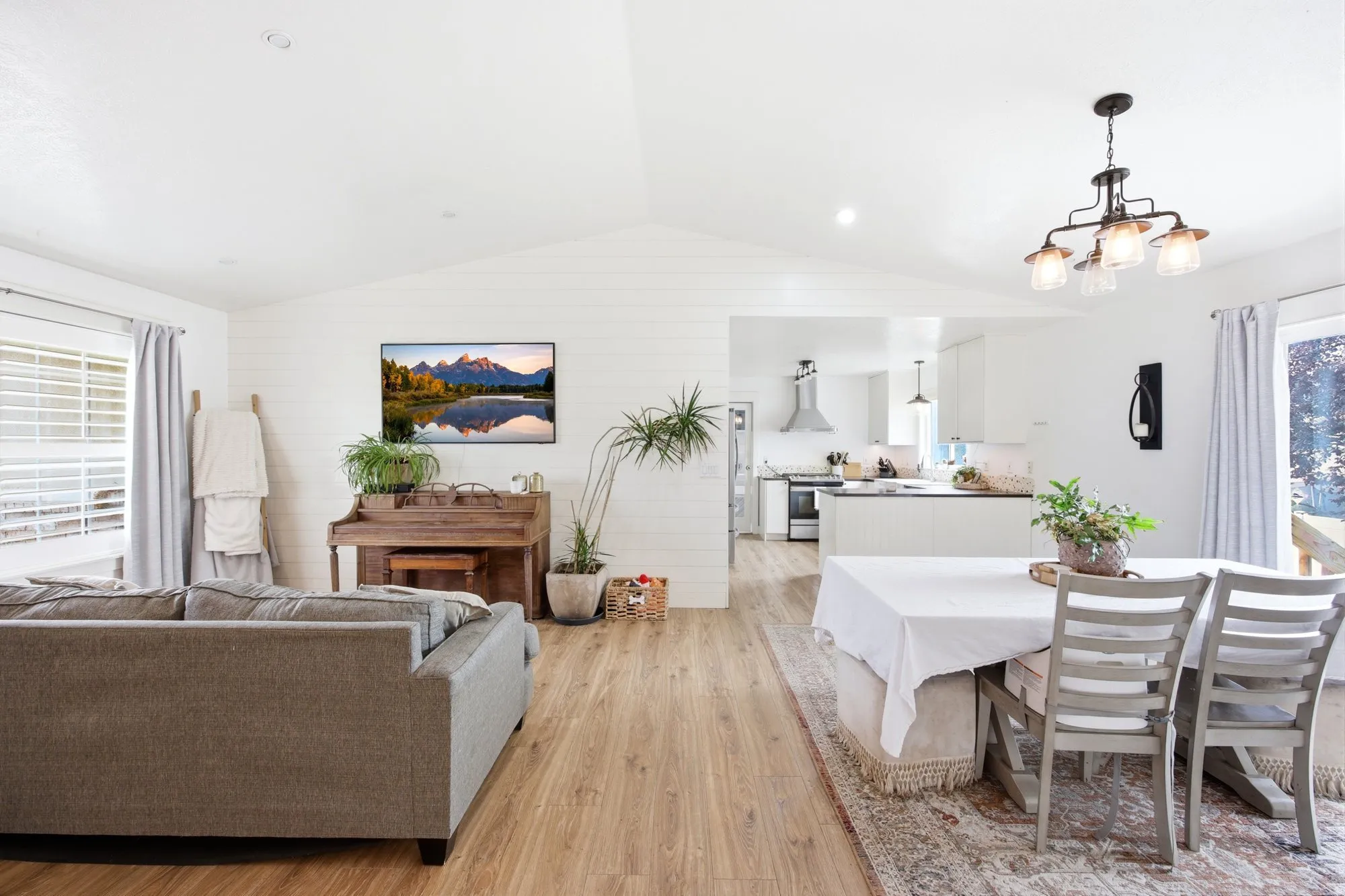Open-concept living area with vaulted ceilings, wood-finish flooring, and white shiplap accent walls