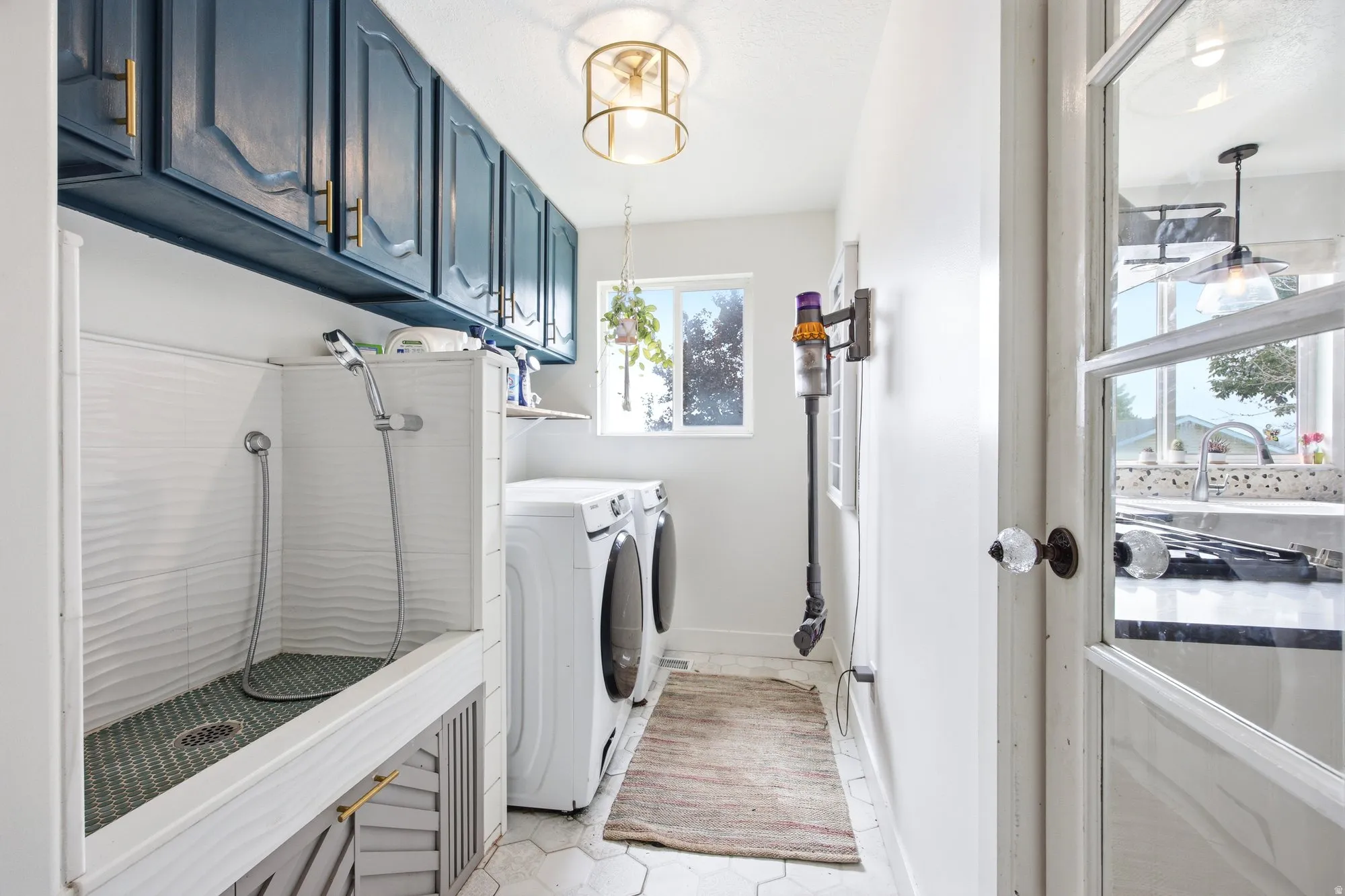 Dedicated utility room featuring a built-in wash station with textured white tile, contrasting blue cabinetry, hexagonal floor tiling, and a window for natural light