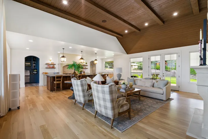Spacious open-concept living area featuring a vaulted wood-finish ceiling with exposed beams, light wood-finish flooring, and a stone fireplace
