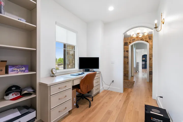 Dedicated workspace featuring wood-finish flooring, a built-in desk with drawers, an arched doorway with stone accents, a sconce, and recessed lighting