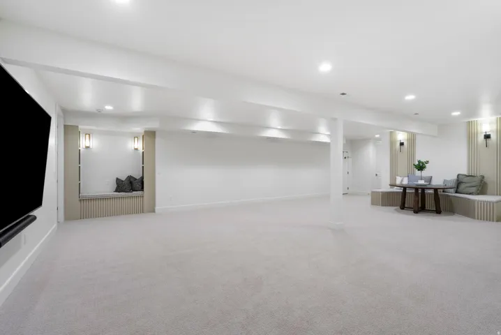Spacious open-concept room featuring light-toned carpeting, recessed ceiling lighting, and built-in seating nooks with accent lighting