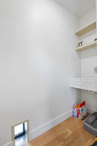 Dedicated pet station featuring wood-finish flooring, a built-in pet door, subway tile-clad pet bathing area, wall-mounted faucet, and floating wood shelves