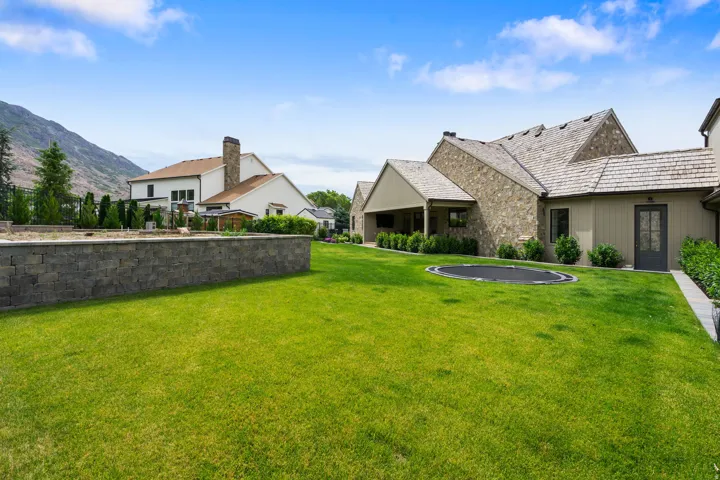 Expansive backyard featuring a manicured lawn, a stone retaining wall, and mountain scenery