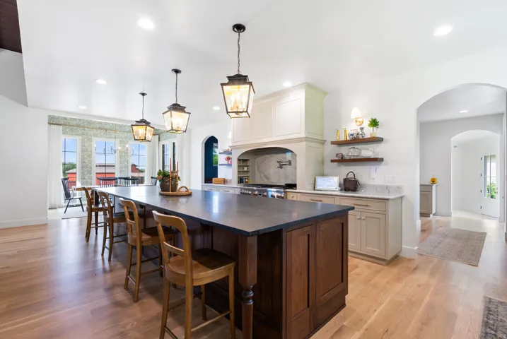Gourmet kitchen featuring a large wood-finish island with seating, a professional-grade range, custom cabinetry, a range hood, and light wood-finish flooring