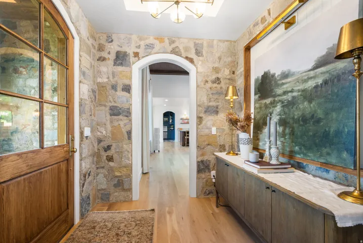 Stone accent wall with an arched doorway opening to light wood-finish flooring