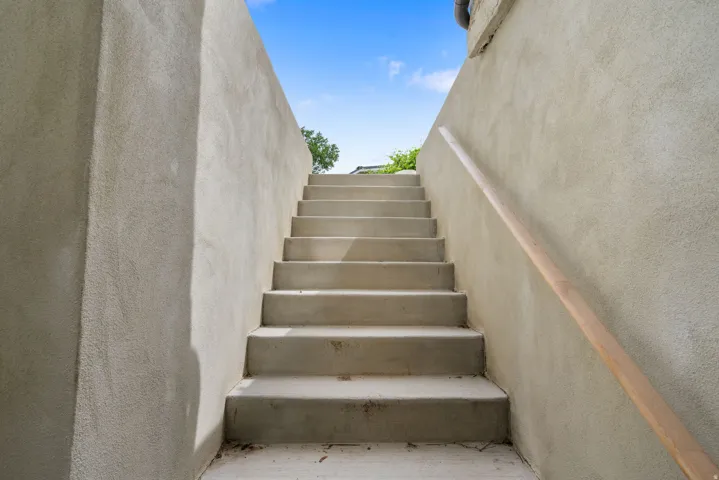 Concrete staircase with textured stucco walls, featuring a natural wood handrail