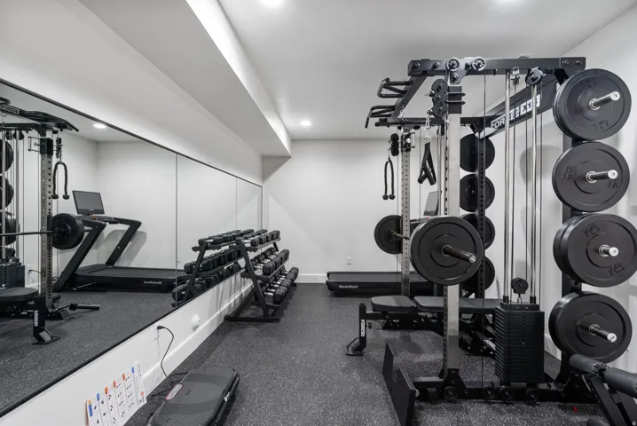 Dedicated fitness space featuring rubber flooring, a mirrored wall, recessed lighting, and white walls
