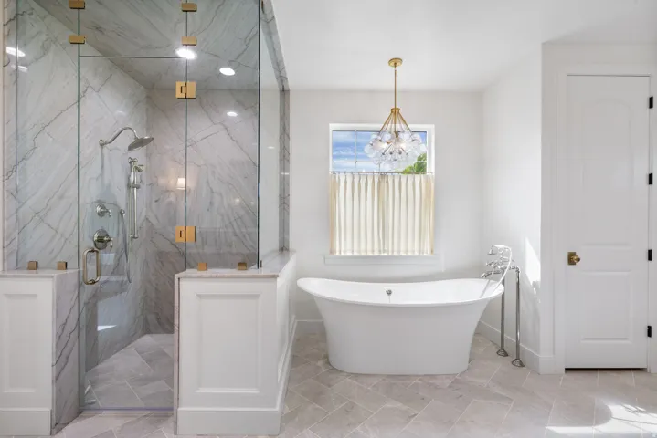 Spacious bathroom featuring a frameless glass shower enclosure with marble-patterned tile, a freestanding soaking tub, and a decorative pendant light fixture