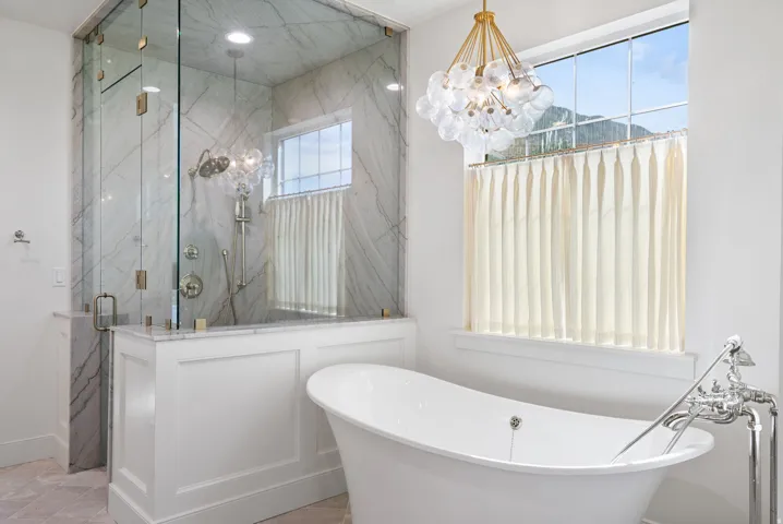 Freestanding soaking tub complemented by a glass-enclosed shower with marble-look wall tile