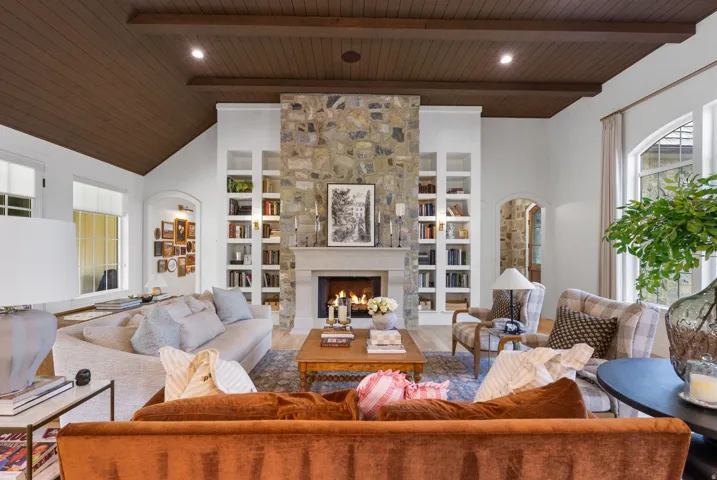 Living area featuring a stone fireplace with a cast stone mantel, built-in shelving, wood-paneled vaulted ceiling, and arched window