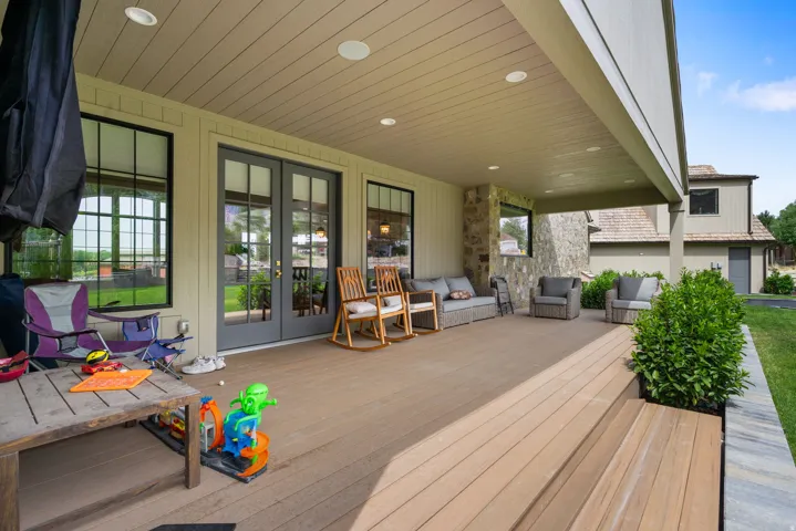 Expansive covered outdoor living space featuring composite decking, recessed lighting, and stone architectural accents