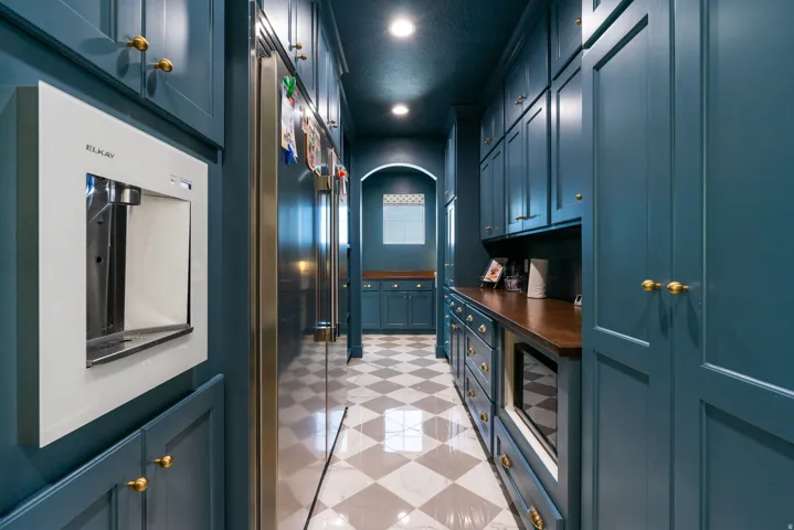Galley kitchen featuring extensive blue cabinetry with brass hardware, stainless steel refrigerators, wood countertops, and checkered tile flooring