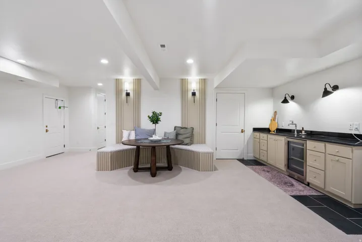 Spacious lower-level area featuring a built-in banquette, recessed lighting, and a wet bar with a beverage cooler