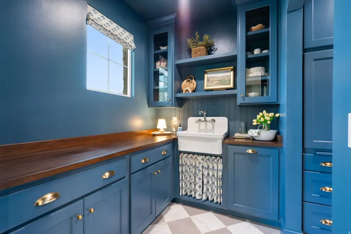 Custom cabinetry with brass hardware, wood-finish countertops, and a built-in utility sink