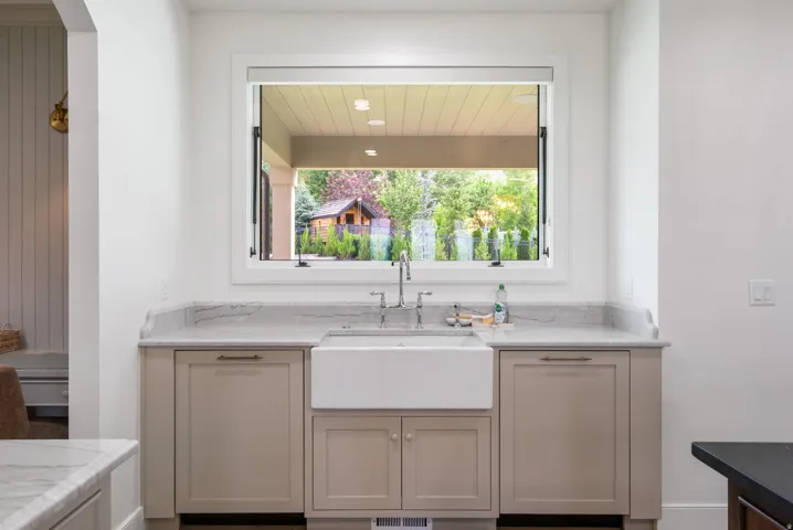 Kitchen window featuring a farmhouse sink, stainless steel faucet, and light-toned cabinetry with coordinating hardware