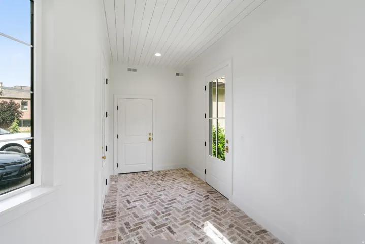 Entryway featuring herringbone brick flooring, crisp white walls, a shiplap ceiling with recessed lighting, an arched panel door, and a glass-paneled exterior door