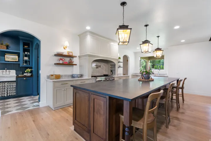Spacious kitchen featuring a large wood-finish island with seating, a range hood over a professional-style range, and light wood-finish flooring