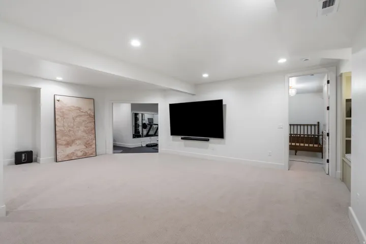 Spacious carpeted room featuring recessed lighting, a large wall-mounted television, and access to additional rooms