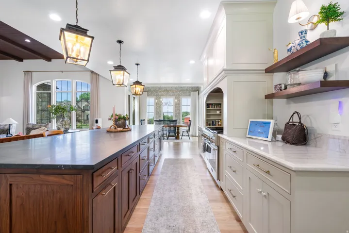 Gourmet kitchen featuring a substantial island with a dark stone countertop and rich wood cabinetry, alongside light-toned perimeter cabinetry with a white stone countertop