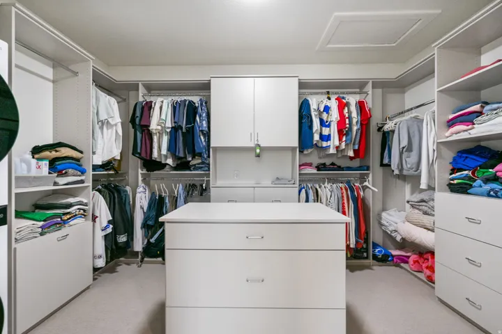 Spacious custom closet featuring extensive shelving, hanging rods, an integrated center island with drawer storage, and built-in cabinetry